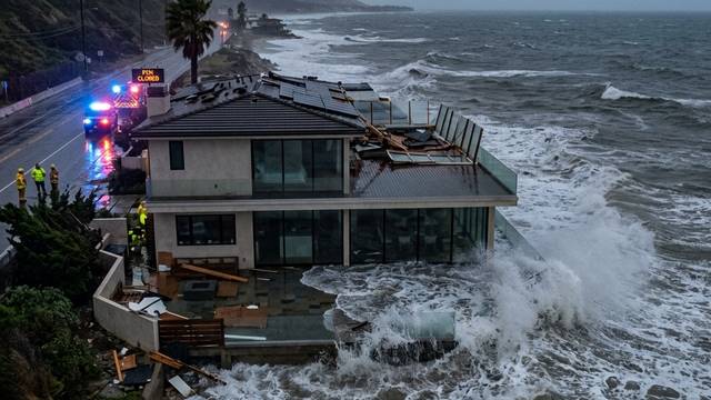 A coastal home with a damaged roof and scattered debris as storm waves hit the structure